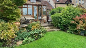 Une maison dotée d’une véranda, d’une pelouse bien entretenue et d’une grande variété de plantes.