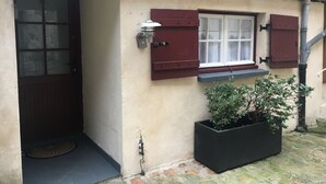 A house with a dark wooden door, a window with red shutters, and a potted plant beside the entrance. - Le Petit Hameau de Chantilly - Chic and Charming Studio in the Heart of Chantilly (CHANTILLY)