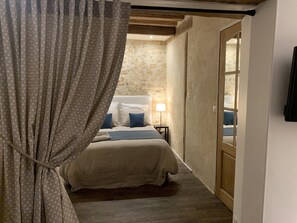 Un dormitorio con cama, mesita de noche, lámpara y vistas a una pared de piedra y una puerta de madera.