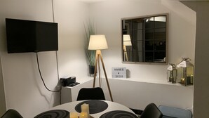 A dining area with a round table, candles, a TV mounted on the wall, a window with a view, and a sign indicating the year 2020. - Le Petit Hameau de Chantilly - Chic and Charming Studio in the Heart of Chantilly (CHANTILLY)