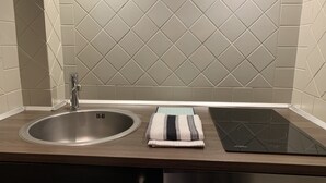 A kitchen with a stainless steel sink, a built-in induction cooktop, and a tiled backsplash. - Le Petit Hameau de Chantilly - Chic and Charming Studio in the Heart of Chantilly (CHANTILLY)