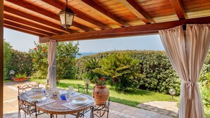 An outdoor patio with a table set for dining, a potted plant, and a view of the sea.
