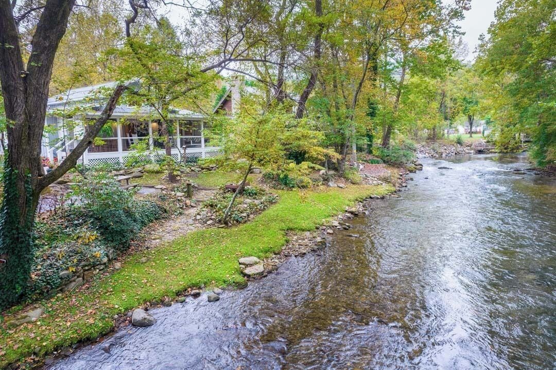 Un río atraviesa un jardín con una casa a la izquierda.