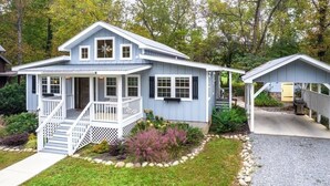 Ein zweistöckiges Haus mit Veranda, überdachtem Sitzbereich und kleiner Garage.