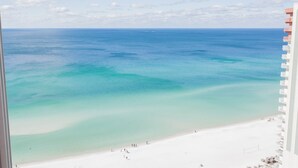 Vista de una playa con agua turquesa cristalina, arena blanca y algunas personas en la orilla.