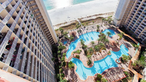 Un hotel de gran altura con piscina en la azotea, vista a la playa y varios balcones.
