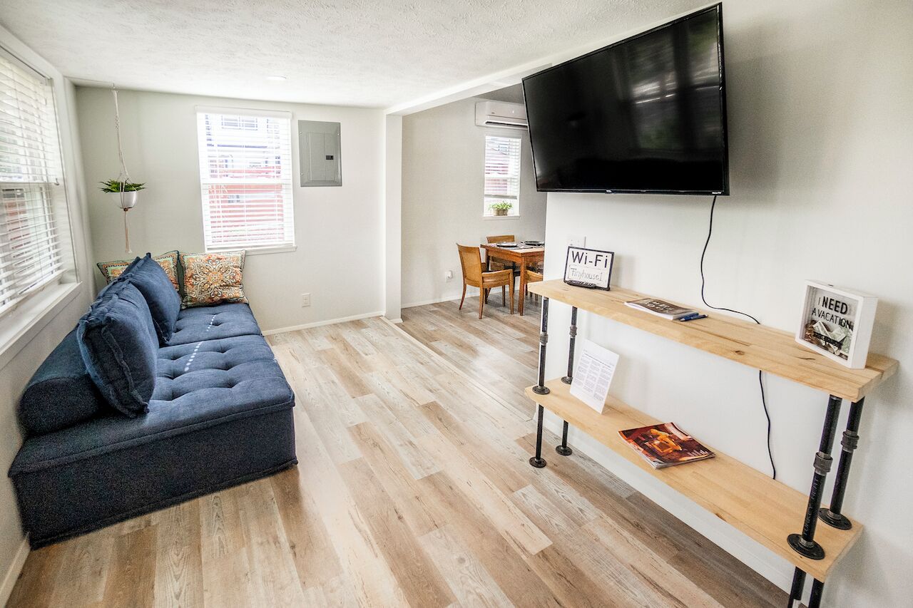 A modern living room with a sofa, a TV mounted on the wall, a wooden table with a Wi-Fi sign, and a bench.
