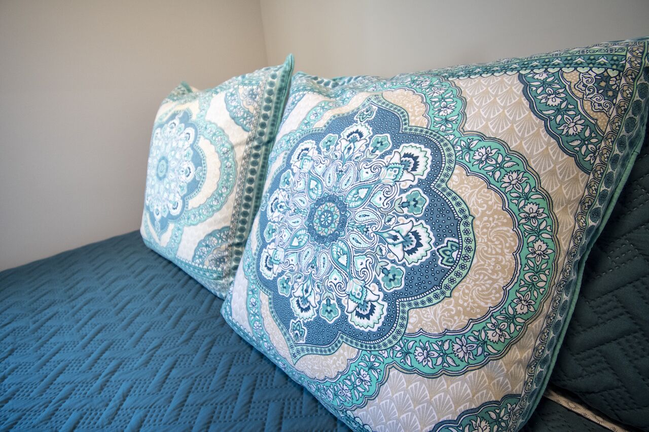 A bed with blue bedding and decorative pillows with intricate patterns.