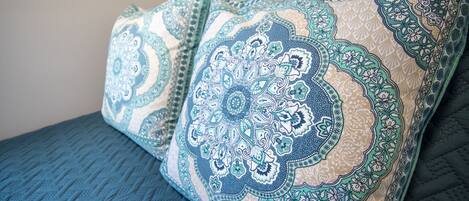 A bed with blue bedding and decorative pillows with intricate patterns.