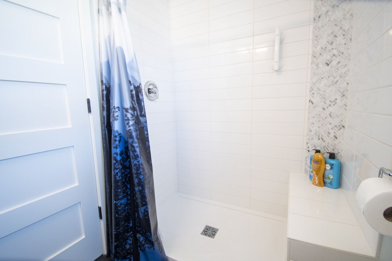 A bathroom with white tiled walls, a shower curtain with a forest pattern, and toiletries on the sink.
