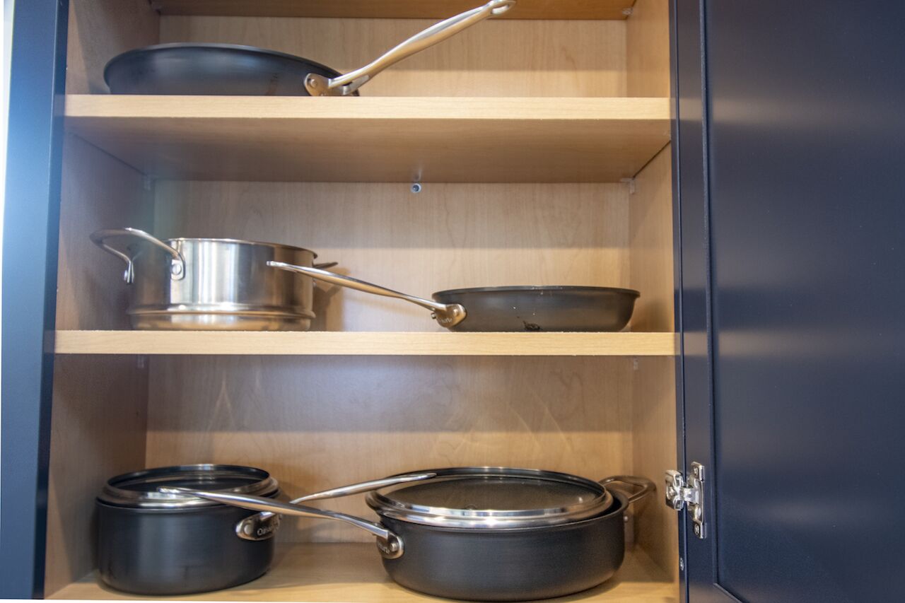 A kitchen cabinet with three shelves, each holding different kitchenware.
