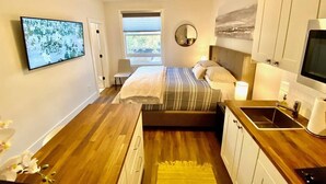 A bedroom with a bed, a ceiling fan, a TV, a window, and a small kitchenette. - 203-Remodeled Studio Downtown San Jose, CA (San Jose)