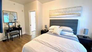 Un dormitorio con una cama grande, un escritorio, una silla y una mesita de noche con una lámpara.