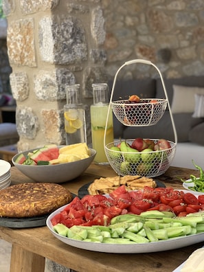 A breakfast spread with various fruits, vegetables, and drinks on a wooden table. - The River House (Ula)