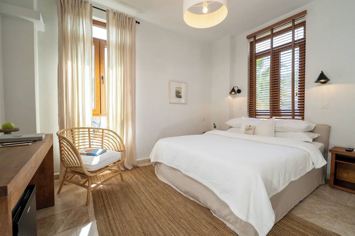 A bedroom with a bed, a desk, a chair, and a window with blinds.