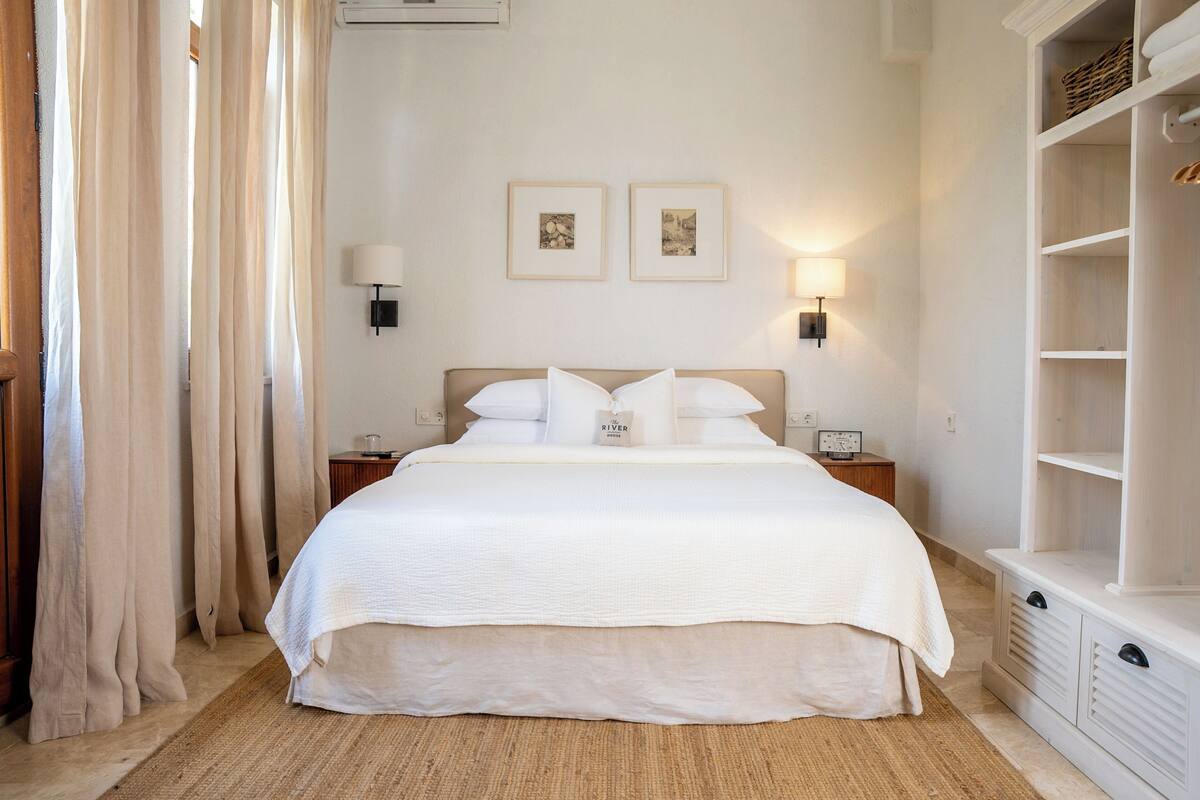 A neatly arranged bedroom with a large bed, bedside lamps, a nightstand, and a wardrobe.