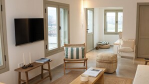 A modern living room with a flat-screen TV, wooden furniture, and a view through a door. - The River House (Ula)