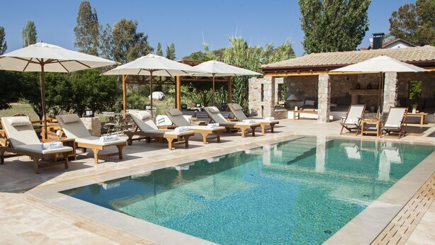 A pool area with lounge chairs and umbrellas, surrounded by stone structures and greenery. - The River House (Ula)