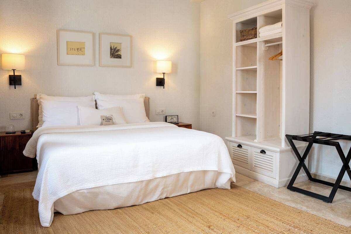A neatly arranged bedroom with a large bed, bedside tables, a wardrobe, and wall-mounted lamps.