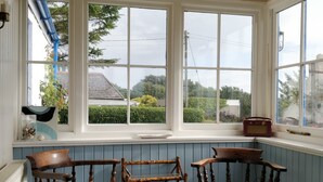 Quarto com janela panorâmica, cadeiras de madeira, uma pequena mesa e uma estante de livros.