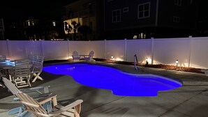 Una piscina iluminada con luz azul, rodeada de sillas blancas y un trineo de madera.