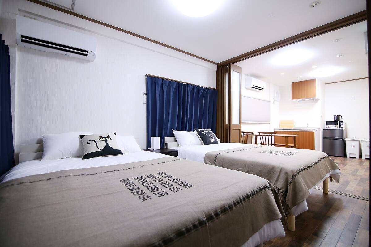 A hotel room with two beds, a kitchenette, and a bathroom visible through an open door.