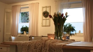 A dining area with a table covered by a lace tablecloth, a vase with flowers, and a window with curtains.