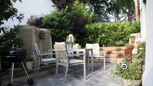 An outdoor patio with a grill, chairs, and potted plants.