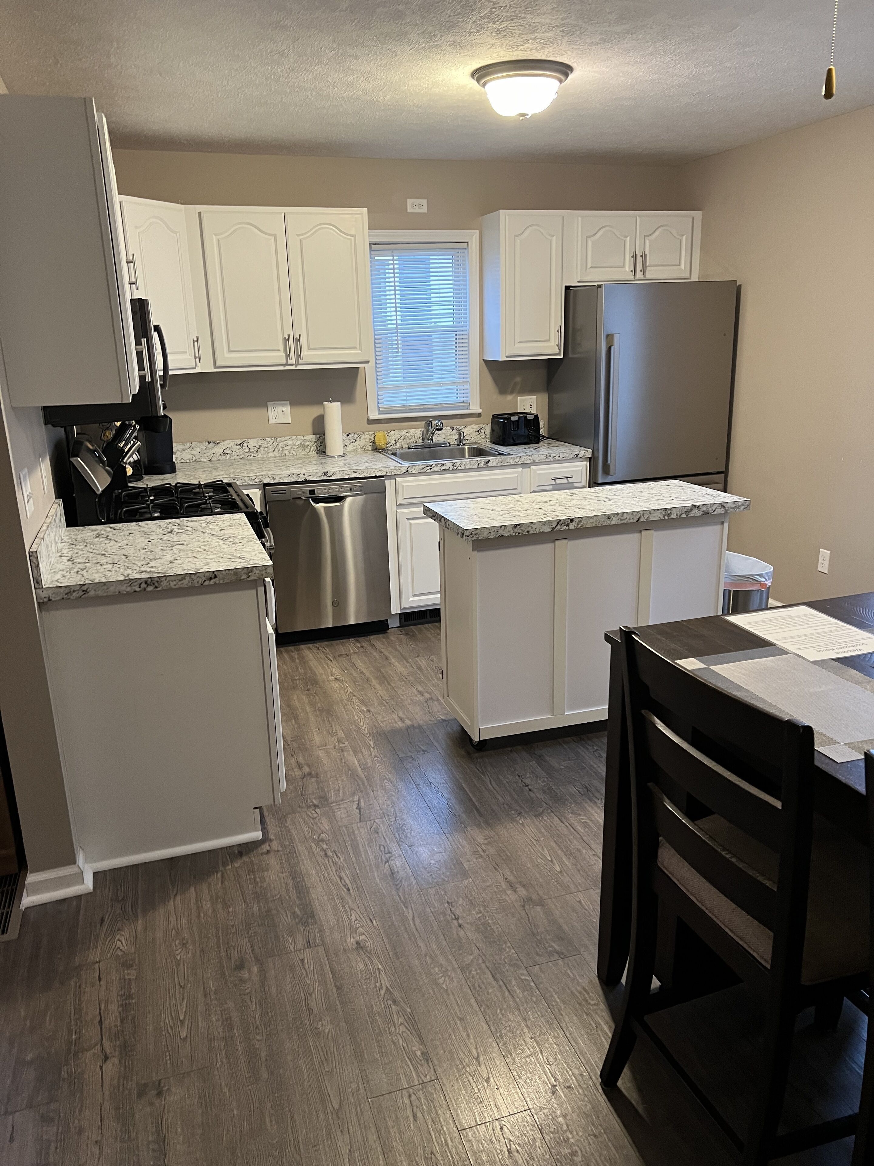 A modern kitchen with white cabinetry, stainless steel appliances, and a marble countertop.