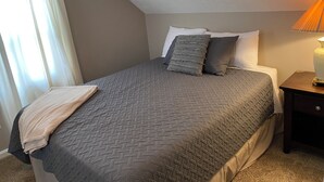 A bedroom with a bed, pillows, a bedside lamp, and a window with curtains. - Relax close to the lakefront! Three bedroom Avon Lake retreat just steps away. (AVON LAKE)