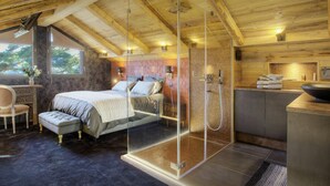 A bedroom with a large bed, a glass shower enclosure, and a small desk with a chair.