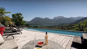 A wooden deck with a pool, lounge chairs, and a table with snacks and a wine bottle.