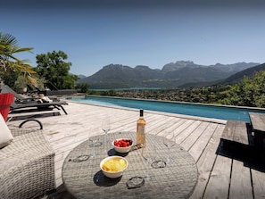 Un pontile in legno con piscina, sedie a sdraio e un tavolo con snack e una bottiglia di vino.