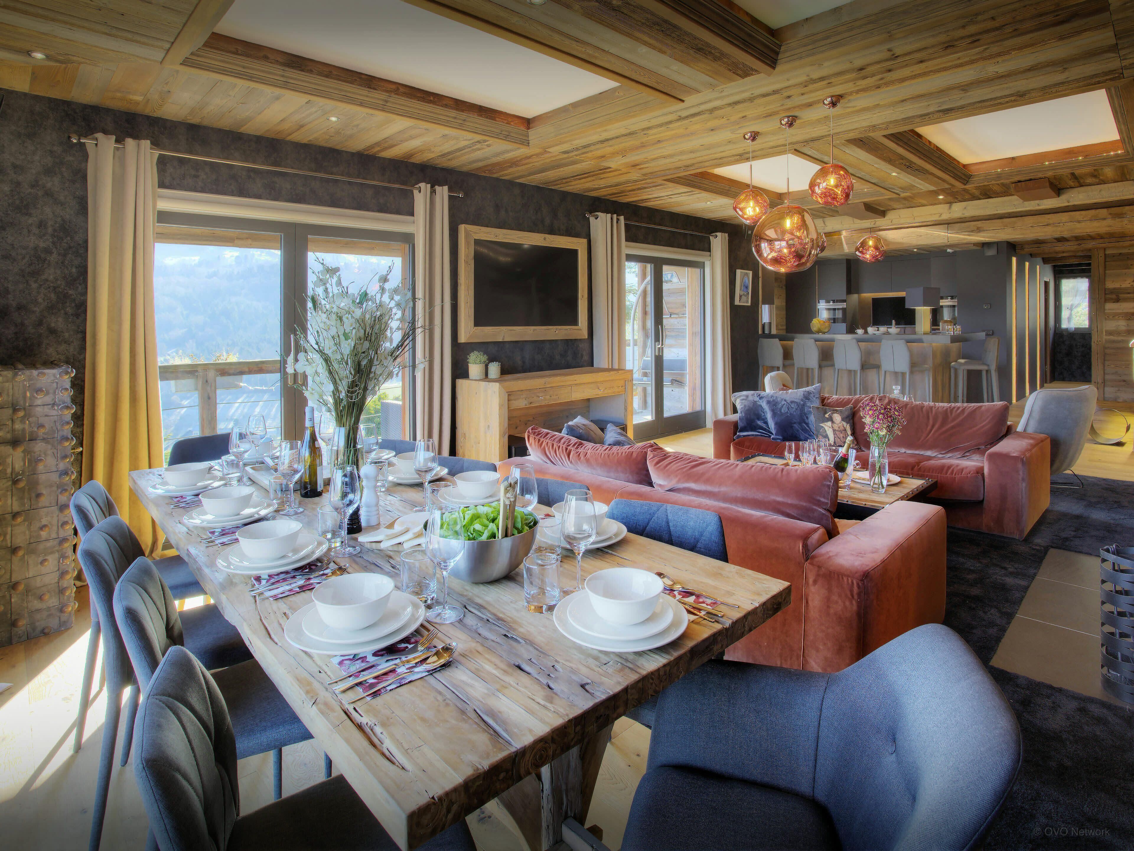 A dining area with a wooden table set for a meal, surrounded by sofas and chairs.