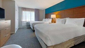 Une chambre d’hôtel avec deux lits, une télévision, un bureau et une fenêtre avec des rideaux.