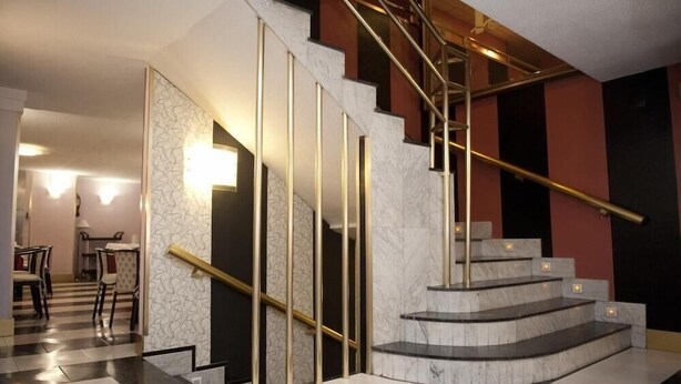 A modern staircase with marble steps and gold handrails, leading to a dining area with tables and chairs. - Arha Santander (Santander)