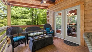 A covered porch with wicker furniture, a ceiling fan, and a view of a forest. - Cute, Cozy Log Cabin, Private setting, Decorated in red & black Rooster theme. (Rogers)