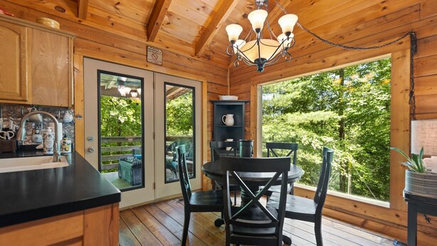 A wooden cabin kitchen with a dining area, large windows, and a view of the forest. - Cute, Cozy Log Cabin, Private setting, Decorated in red & black Rooster theme. (Rogers)