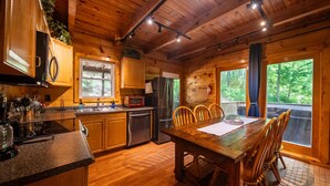 Cucina in legno con tavolo e sedie, frigorifero, lavello e finestra con vista sul verde.