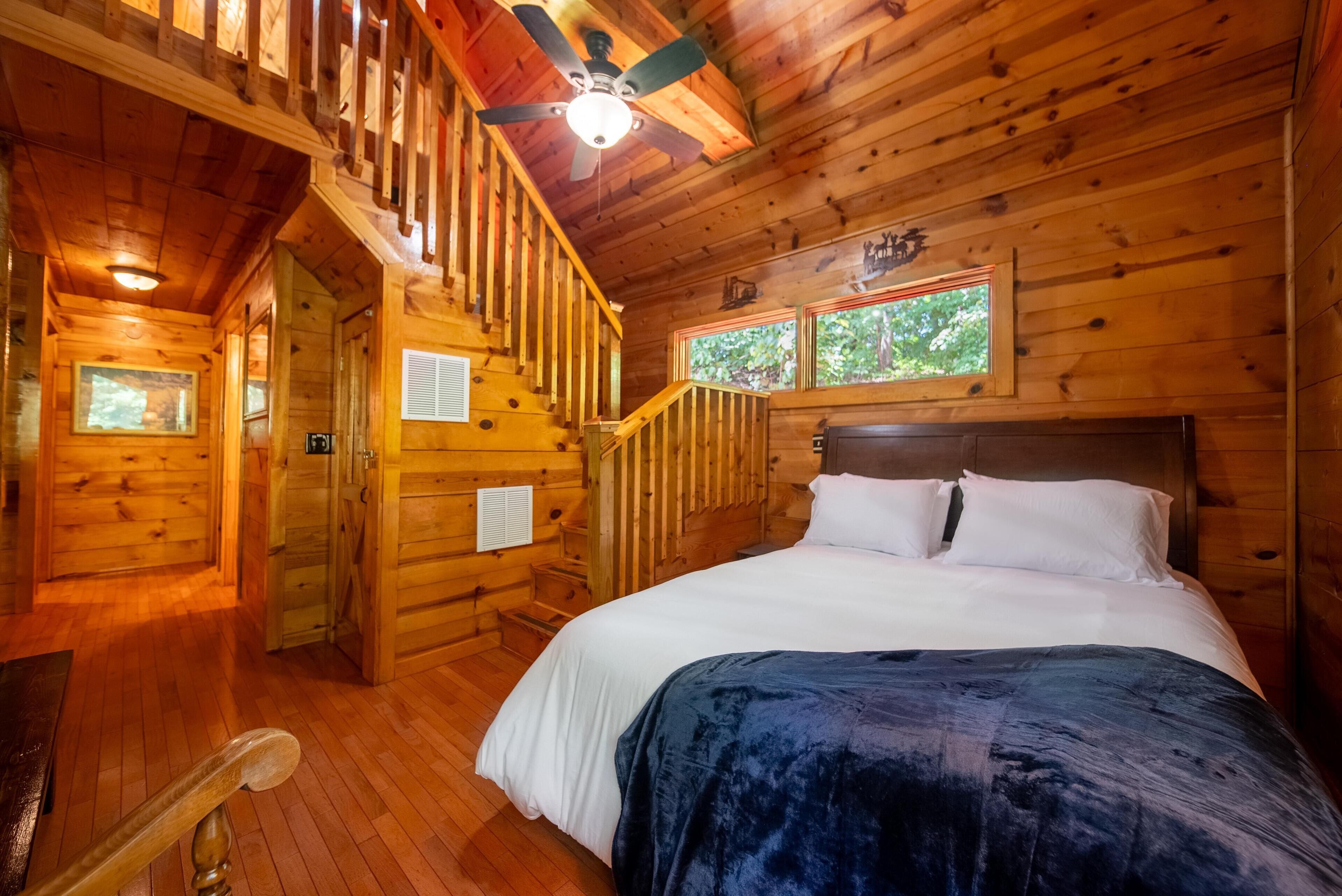 Interior de una cabaña de madera con una cama, una escalera y un ventilador de techo.