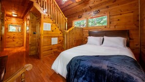 Interno di una baita in legno con un letto, una scala e una ventola a soffitto.