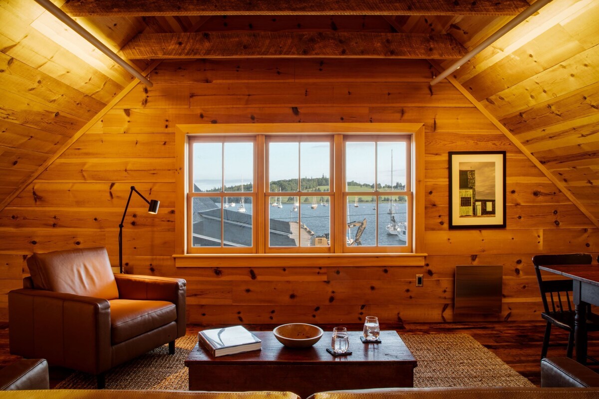 Ein gemütliches Holzhaus mit einem großen Fenster, das einen Blick auf einen Yachthafen bietet.