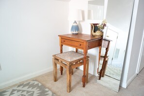 A cozy space with a desk, chair, and vase with flowers, set against a white wall.