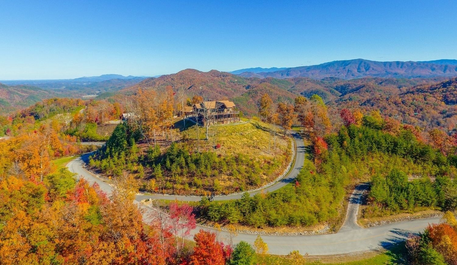 A large house surrounded by a winding road and autumn-colored trees.