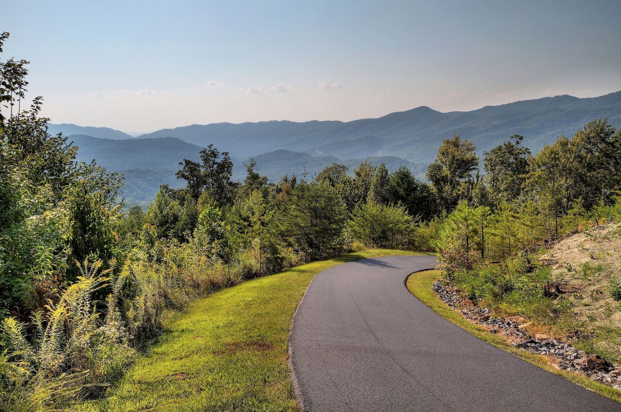A winding road through a mountainous area with lush greenery and distant hills.