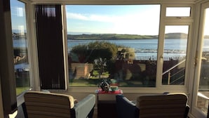 Ett rum med utsikt över en sjö och kullar, inrett med två randiga stolar och ett litet bord med teservis.
