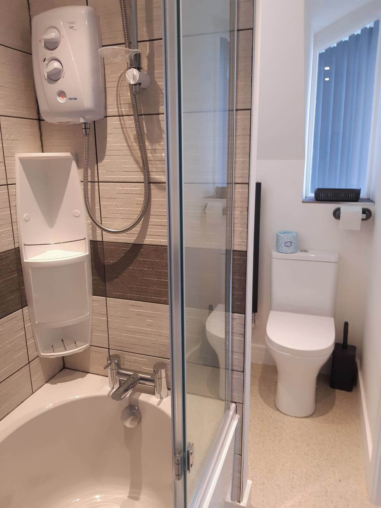 A modern bathroom with a glass-enclosed shower, a white bathtub, and a toilet.