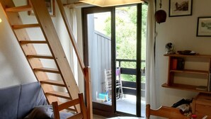 A cozy room with a wooden staircase, a dining table with chairs, a sofa, and a view through a glass door to an outdoor area.
