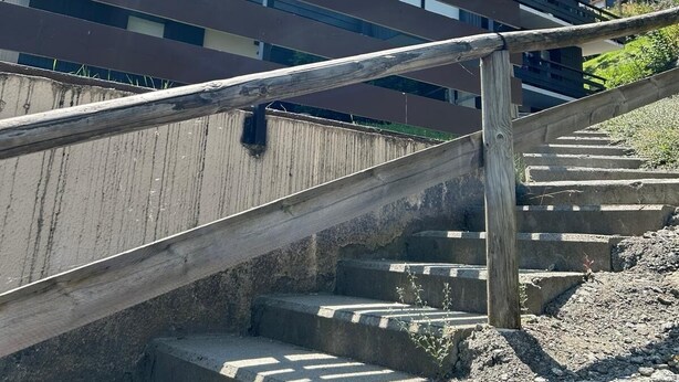 A multi-story building with a modern architectural design, featuring a wooden staircase leading to the entrance.
