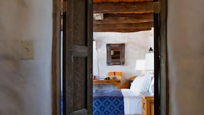 Un estrecho pasillo da acceso a un dormitorio con cama, mesita de noche, lámpara y un espejo colgado en la pared.